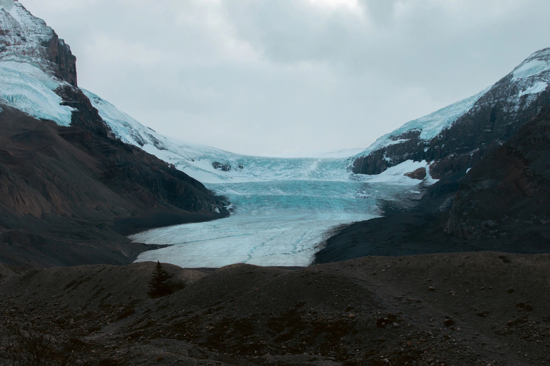Remote alpine glacier between snow-capped mountains under a cloudy sky